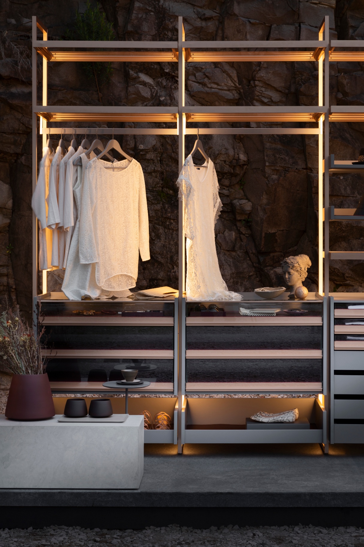 Open-air closet with backlit shelving against rock wall