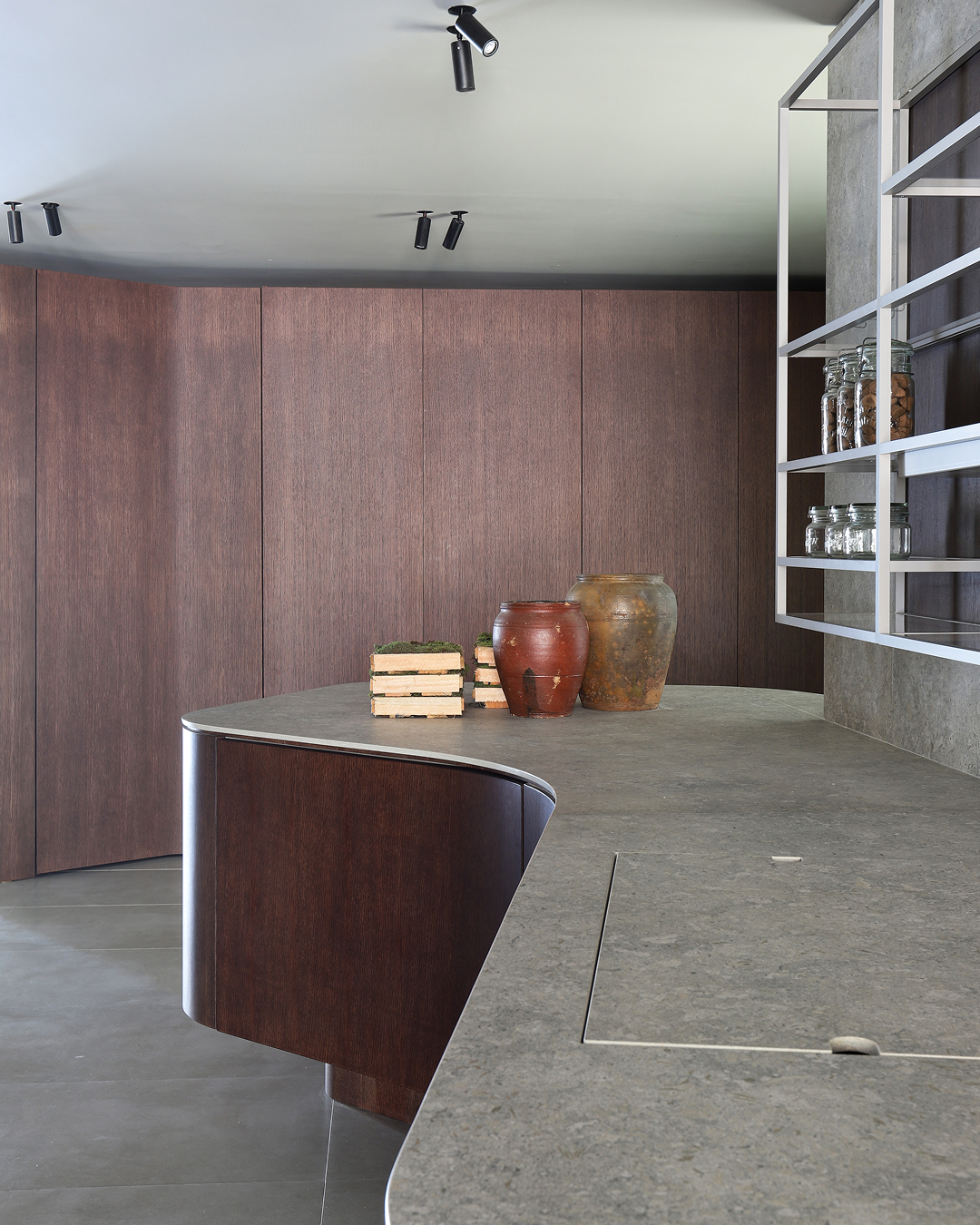 Curved wood island with stone countertop and minimalist shelving